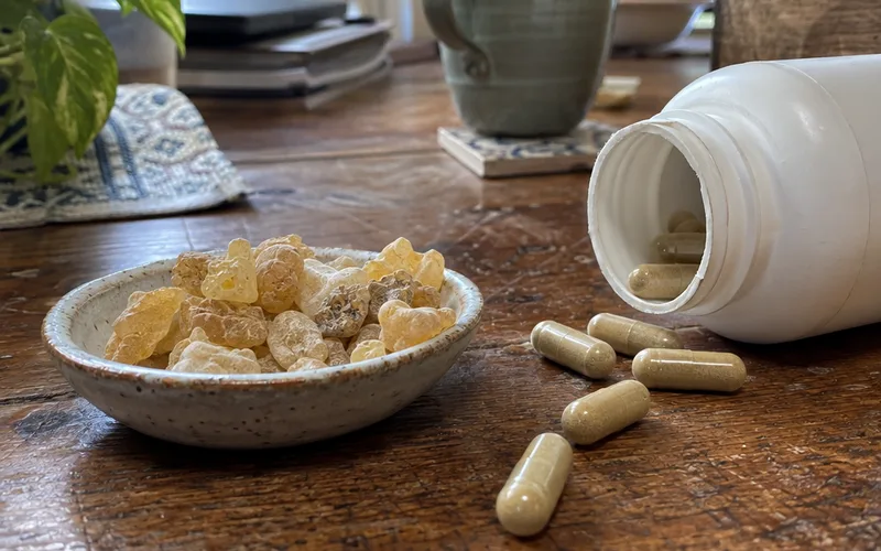 Boswellia supplement capsules spilled from a bottle next to a dish of frankincense resin tears
