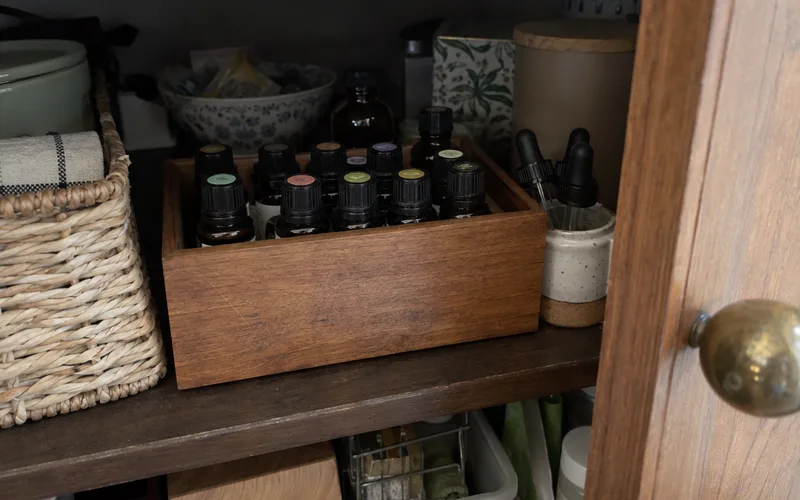 Tightly capped amber essential oil bottles standing upright in a wooden box inside a shaded cupboard
