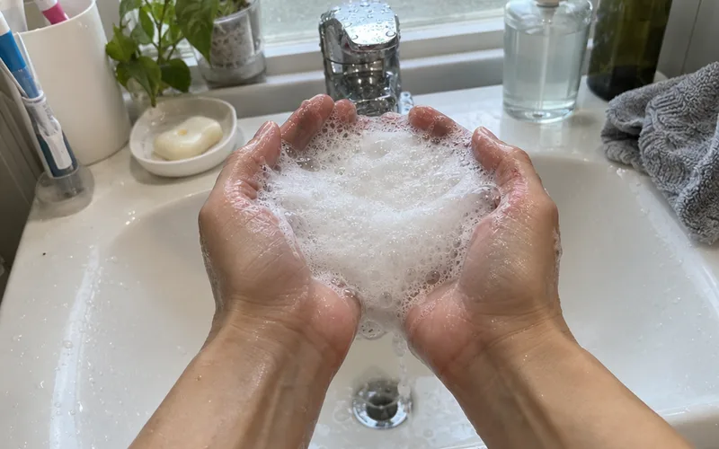Wet cupped hands holding a thick white shampoo lather over a bathroom sink