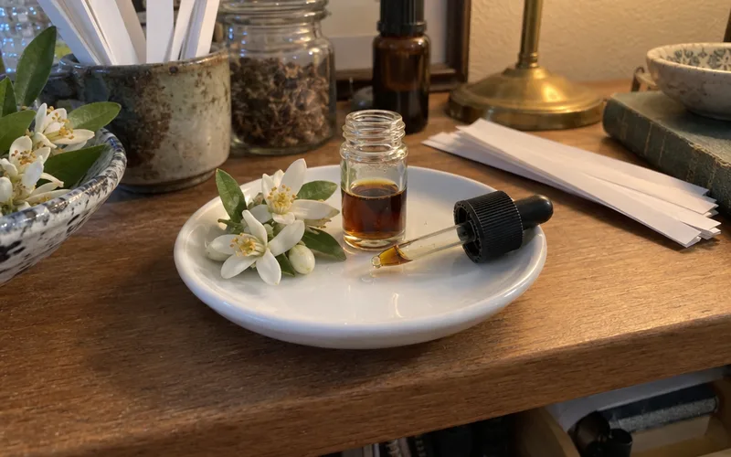 Small glass vial of dark orange blossom absolute next to fresh orange blossoms